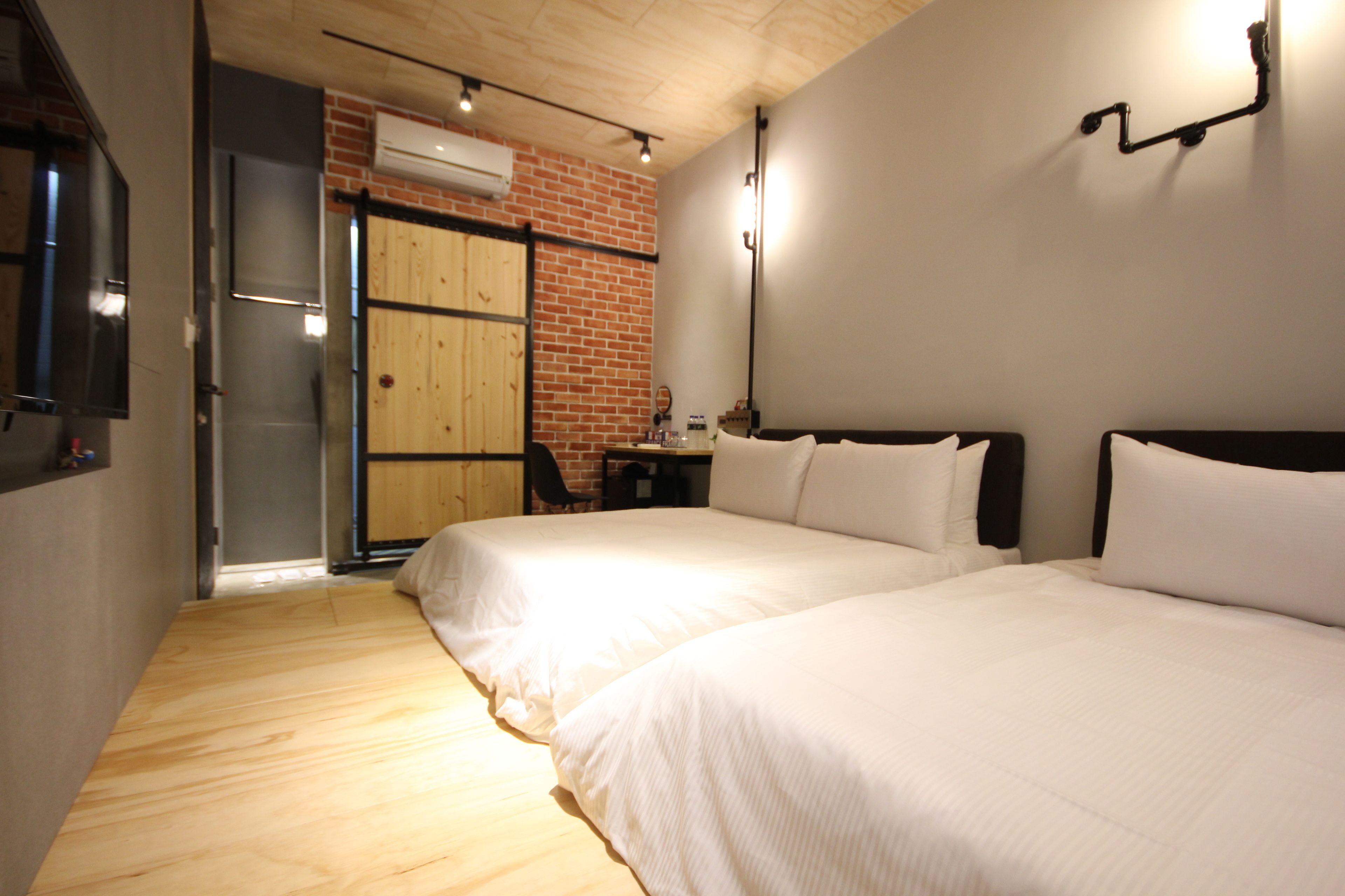 Una habitación con dos camas, piso de madera, pared de ladrillo y una puerta que da a un balcón.