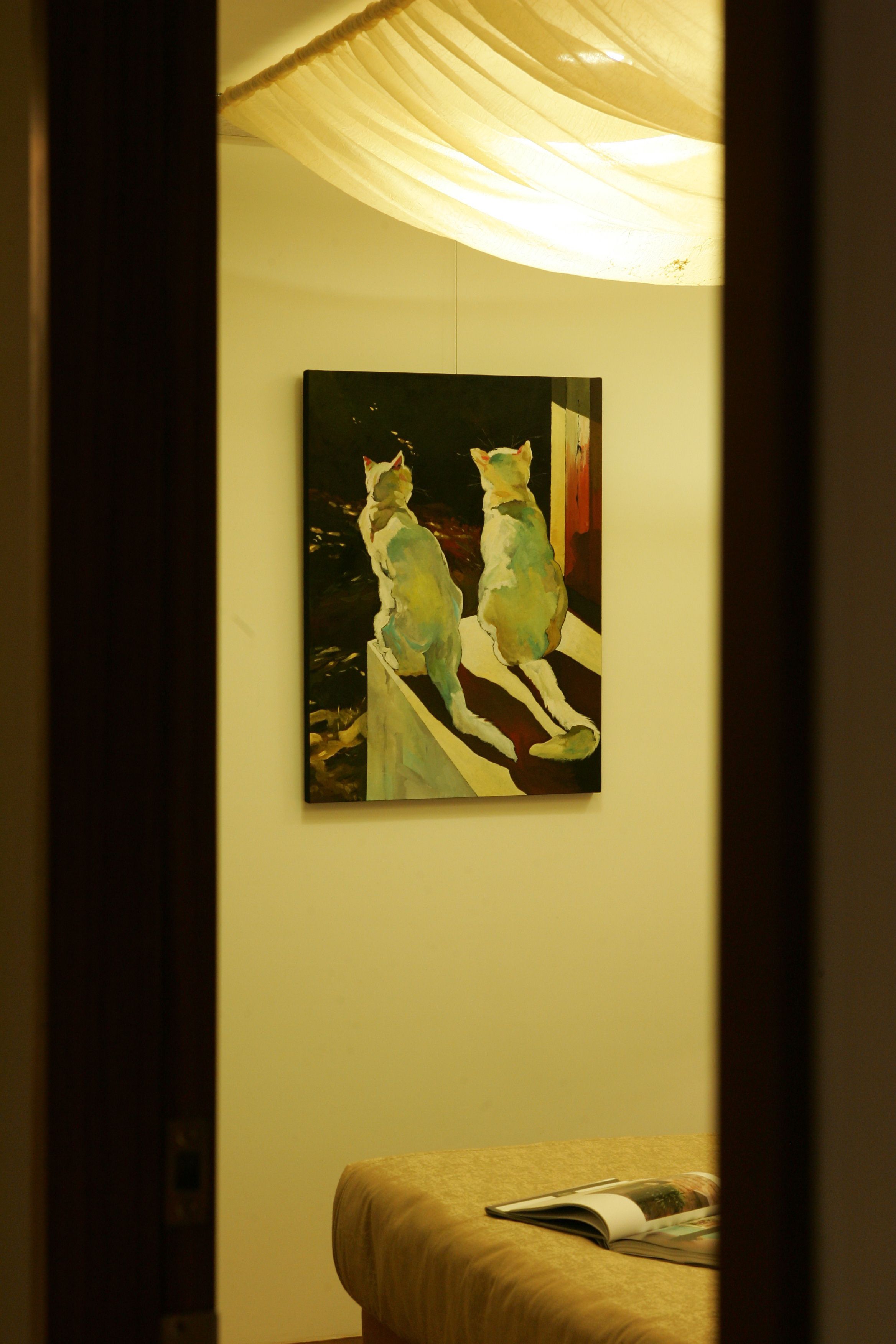 A painting of two cats on a ledge, a bed with a magazine, and a curtain.