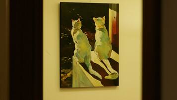 A painting of two cats on a ledge, a bed with a magazine, and a curtain.