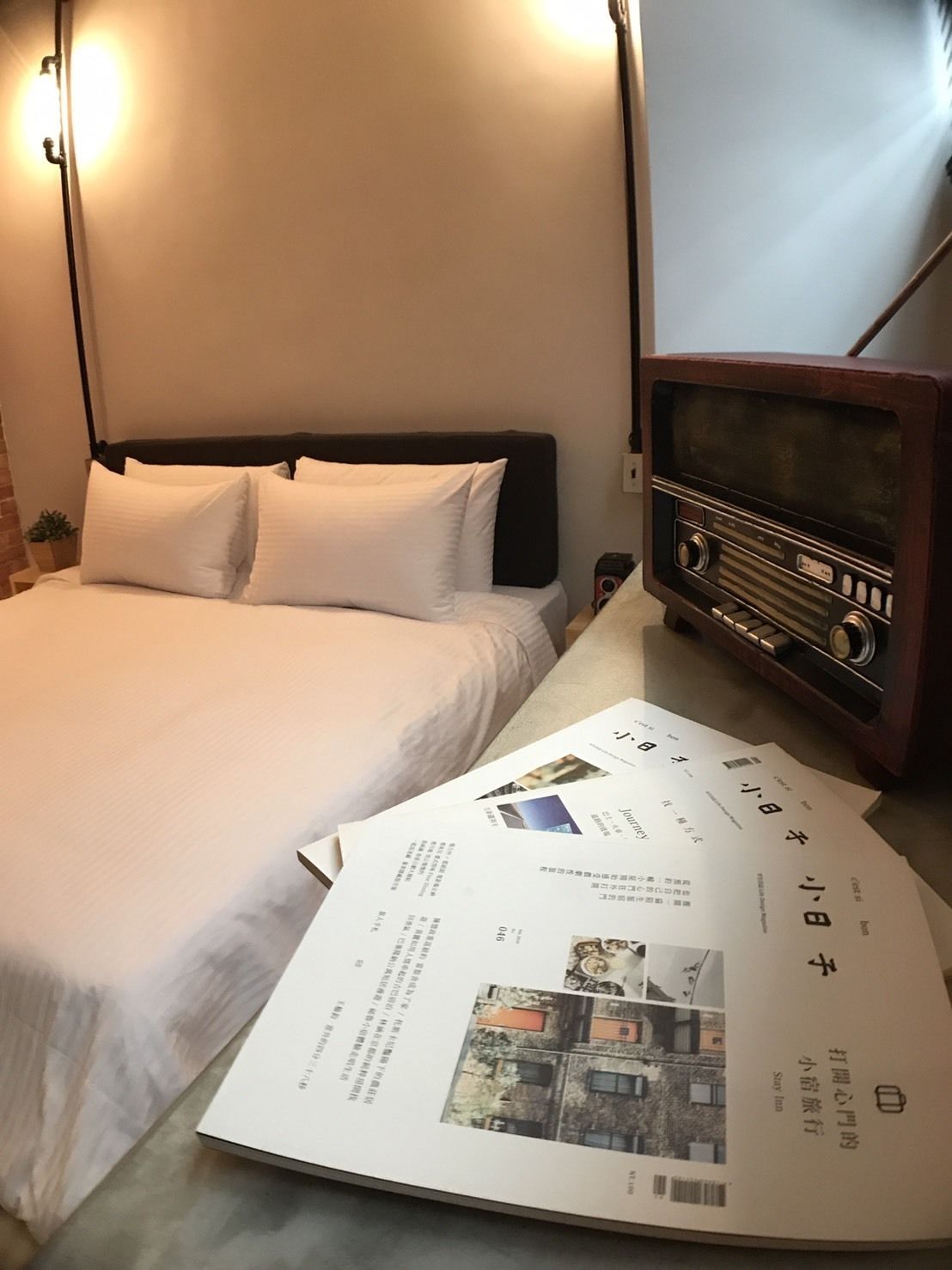 Una habitación de hotel con una cama, una radio de madera y algunos papeles en el suelo.