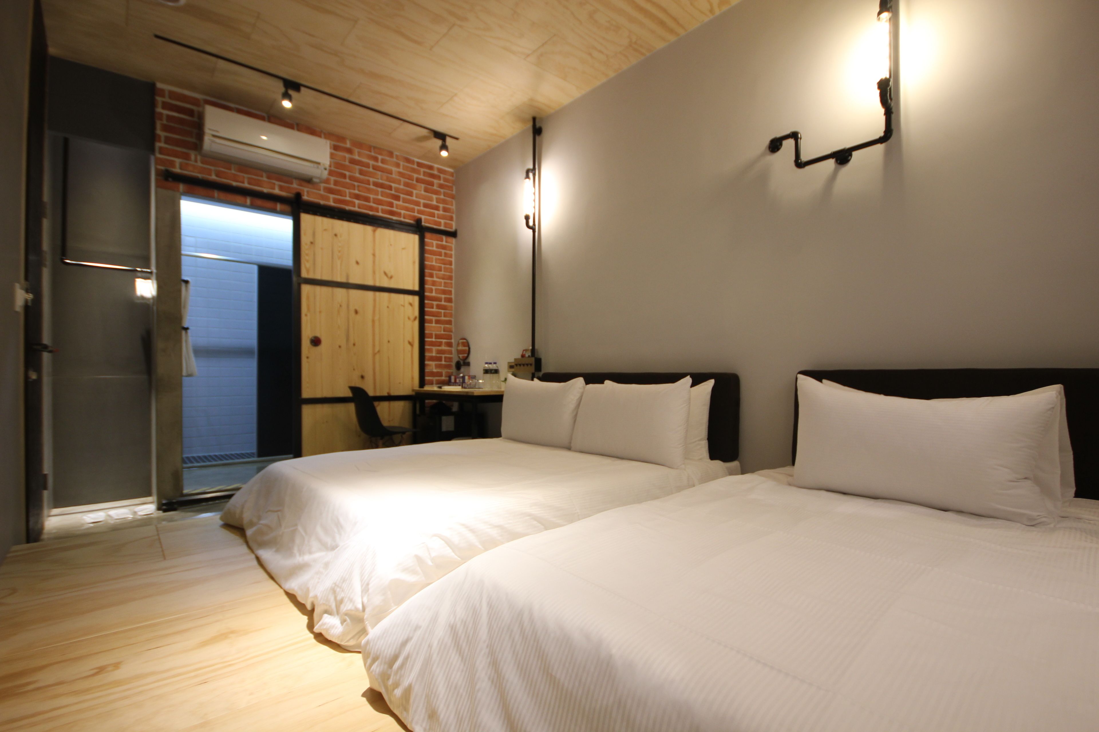 Habitación de hotel con dos camas, una pared de ladrillo y un balcón al que se accede por una puerta corrediza.