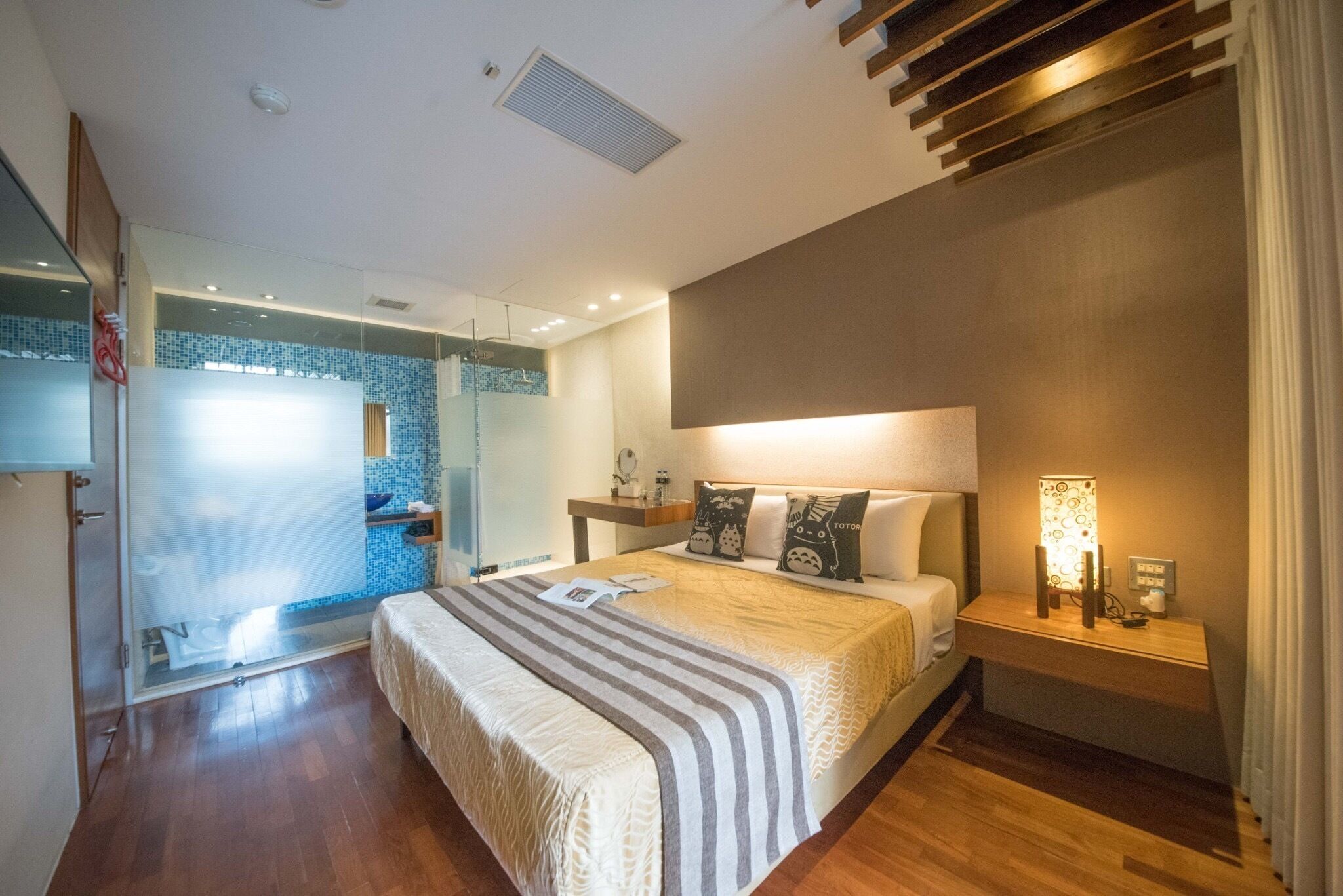 Un dormitorio moderno con una cama grande, una mesita de noche con lámpara, cabina de ducha de vidrio y techo de madera.