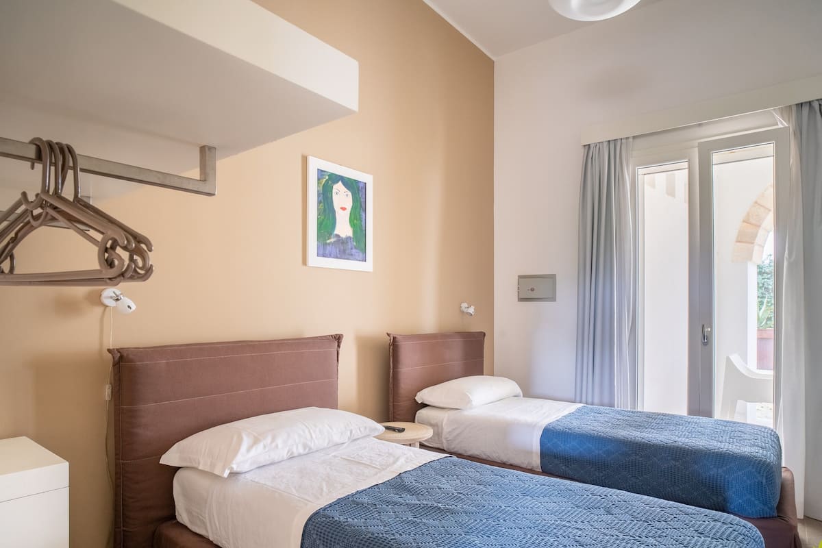 A hotel room with two beds, a painting on the wall, and a view of the outdoors through the window.