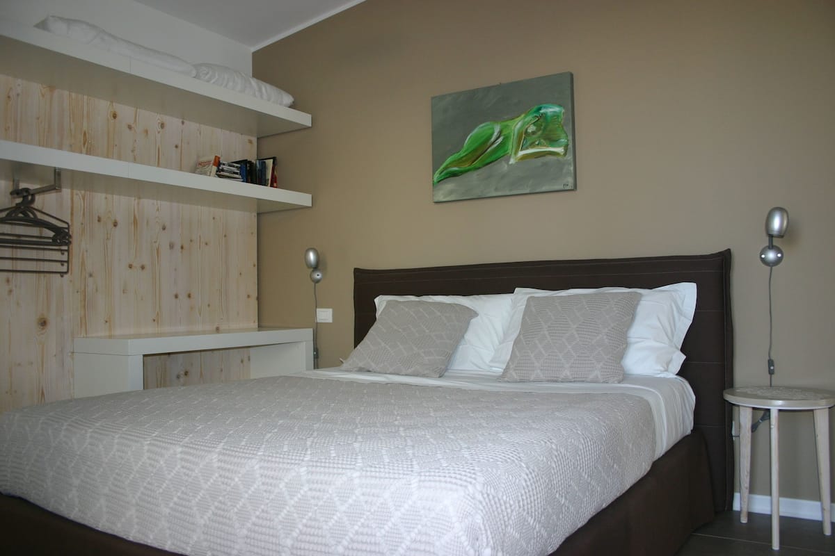 A bedroom with a bed, a wooden wardrobe, a painting, and a bedside table.