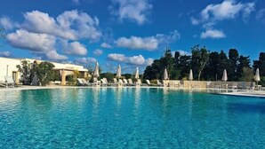 A clear blue pool with lounge chairs and umbrellas, surrounded by trees and a building. - Tenuta Vigna Corallo (Otranto)