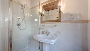 Un baño con cabina de ducha de vidrio, lavamanos blanco y espejo con marco de madera.
