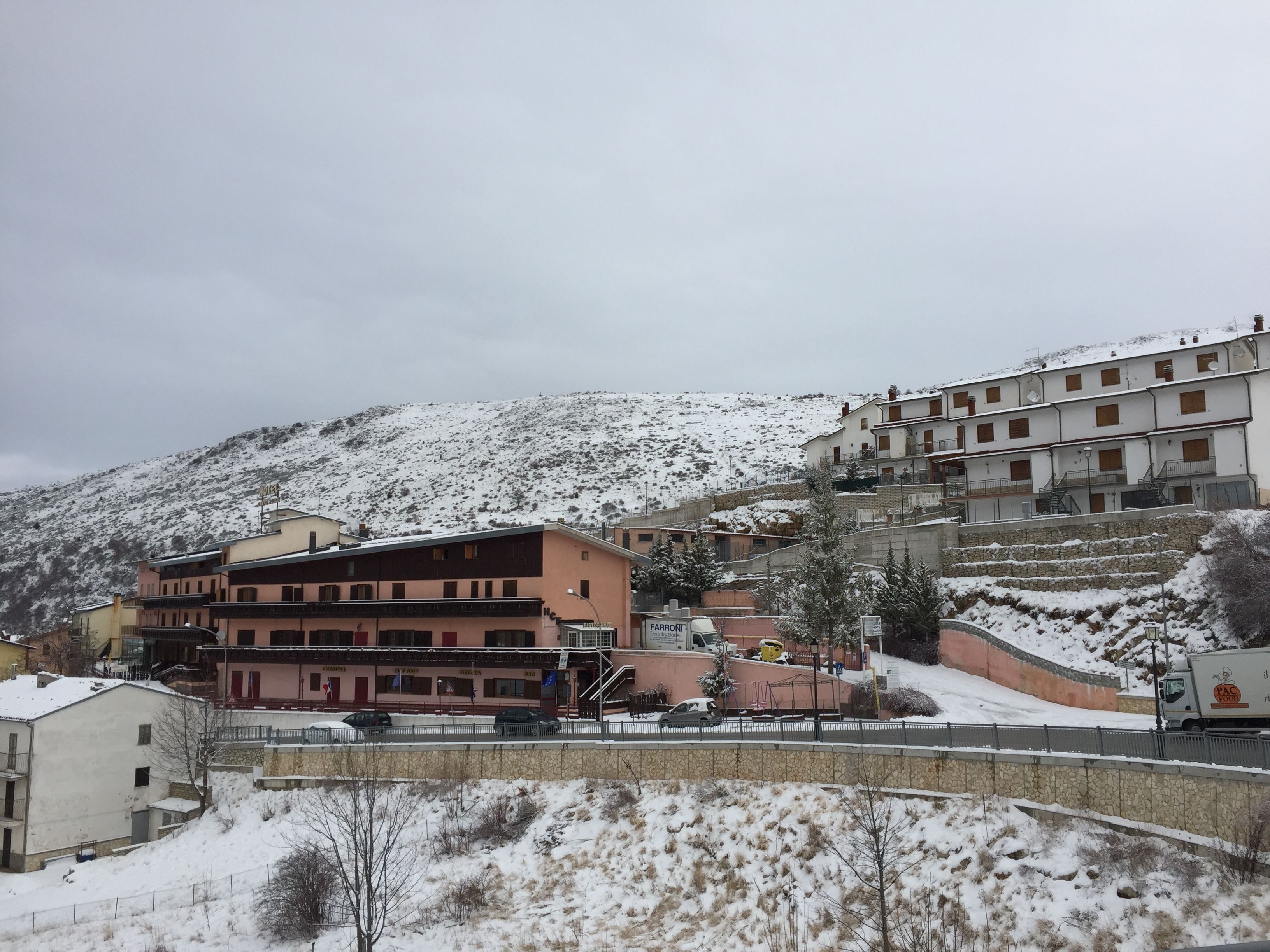 Ein mehrstöckiges Gebäude mit flachem Dach und Balkonen, umgeben von schneebedeckten Hügeln.