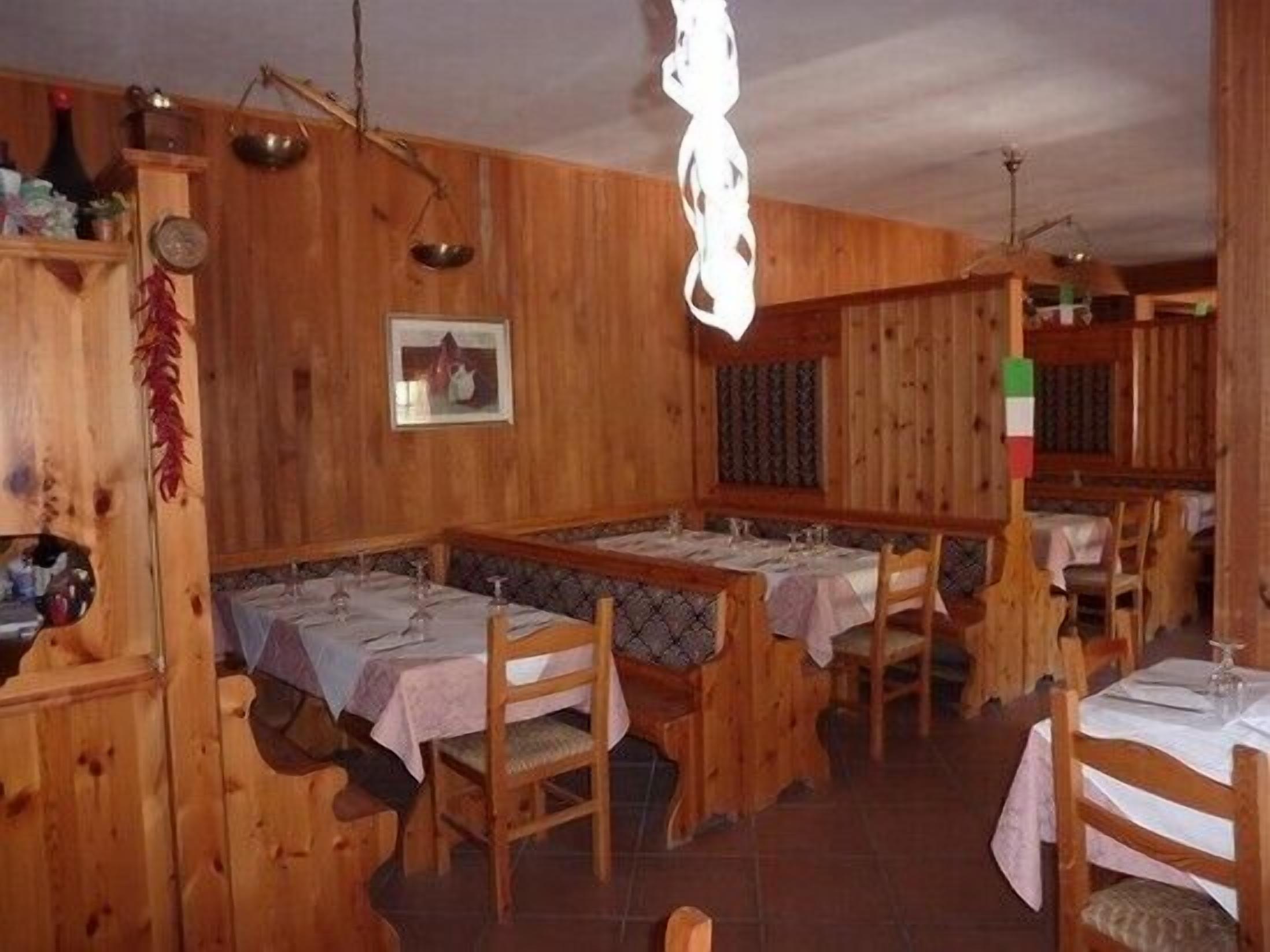 A rustic wooden dining area with multiple tables and benches, a hanging light fixture, and a wall-mounted scale.