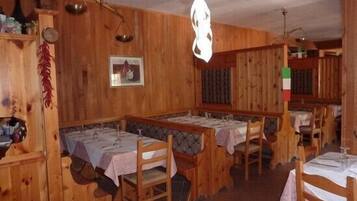 A rustic wooden dining area with multiple tables and benches, a hanging light fixture, and a wall-mounted scale.