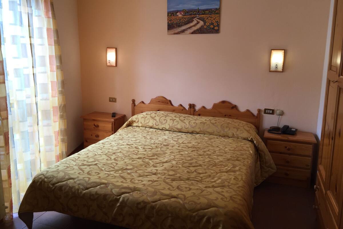 A bedroom with a bed, nightstands, a painting on the wall, and a window with curtains.