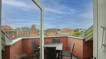 Ein Balkon mit Tisch und Stühlen, ein Holzdeck und ein Blick auf Gebäude in der Ferne.
