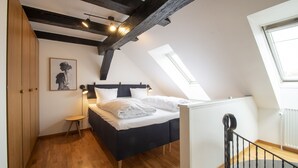 Un dormitorio con cama, una mesita, una mesita de noche, un cuadro en la pared y un tragaluz.