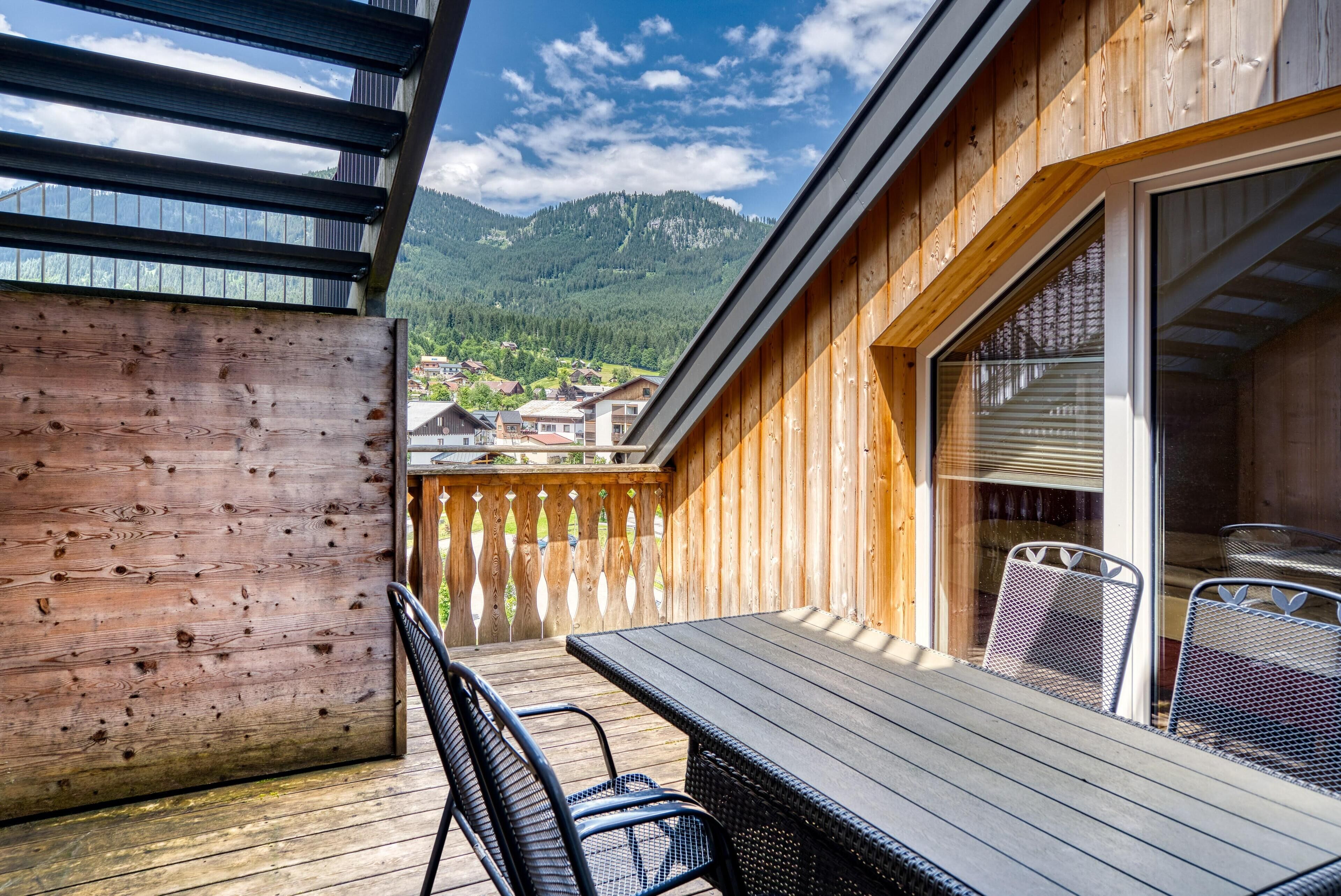 A wooden deck with a table and chairs, overlooking a mountainous landscape.