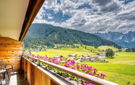 A wooden balcony with a view of a green valley and mountains.