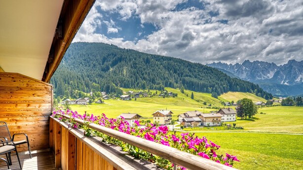 Un balcón de madera con vistas a un valle verde y montañas.