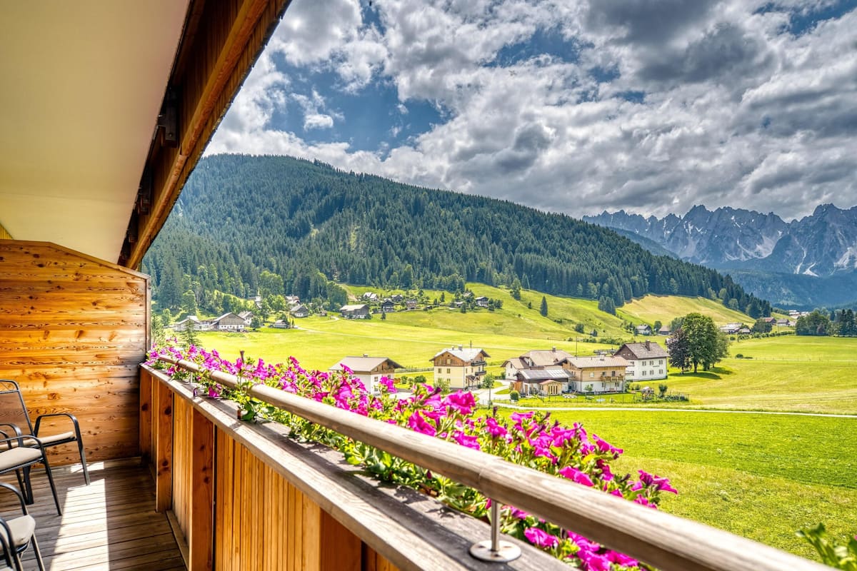 A wooden balcony with a view of a green valley and mountains.