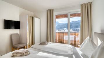 A hotel room with two beds, a TV, a chair, and a balcony with a mountain view.