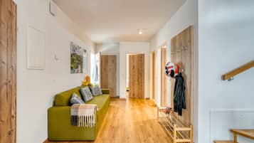 Una sala de estar moderna con un sofá verde, piso de madera y un perchero con chaquetas.