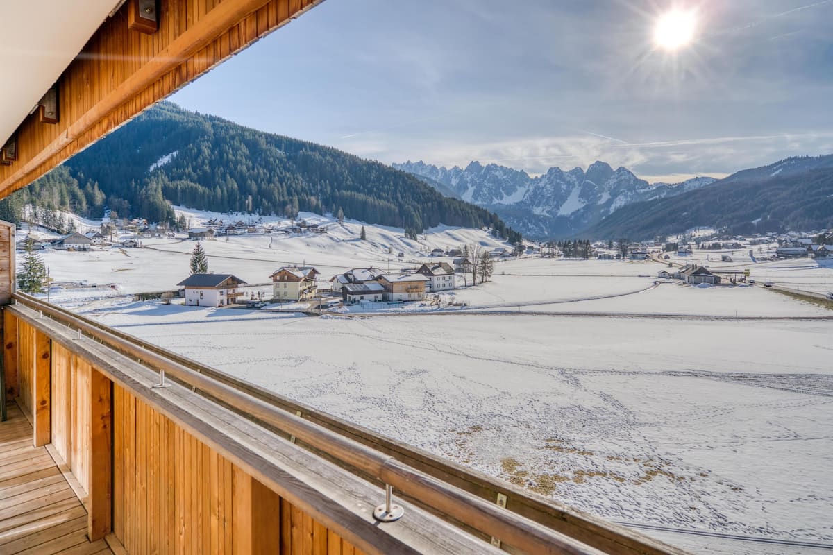A wooden balcony overlooking a snow-covered village with mountains in the background.