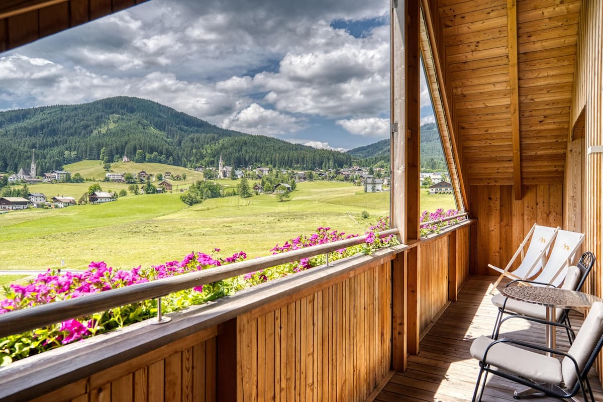 A wooden balcony with a view of a green valley and mountains.