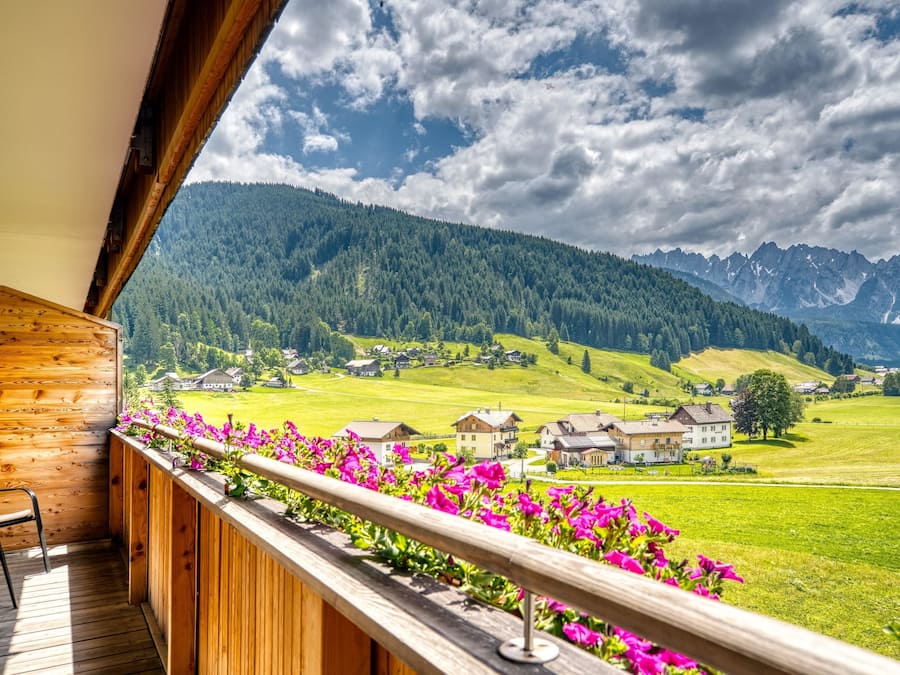 A wooden balcony with a view of a green valley and mountains.