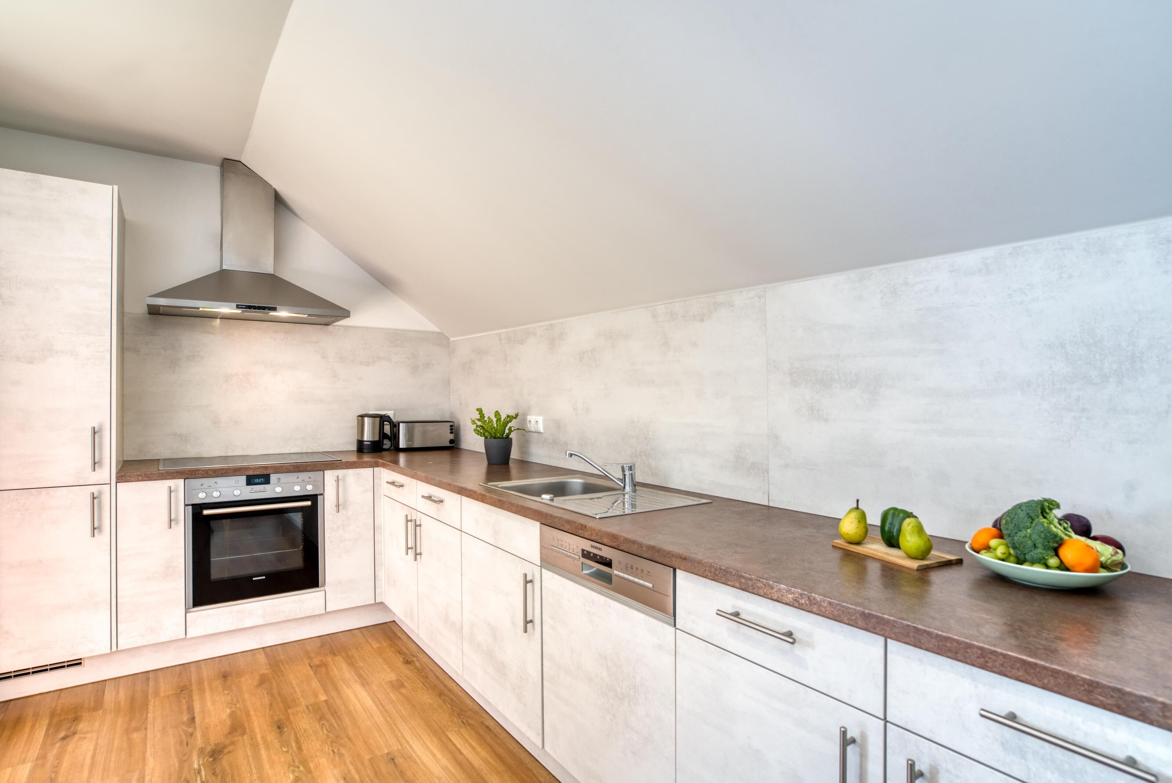 A modern kitchen with white cabinets, a stainless steel range hood, a built-in oven, a dishwasher, and a granite countertop.