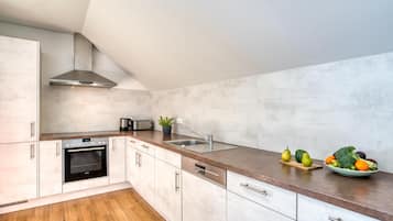 A modern kitchen with white cabinets, a stainless steel range hood, a built-in oven, a dishwasher, and a granite countertop.