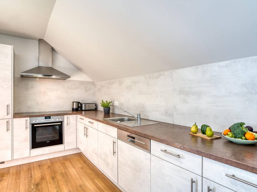 A modern kitchen with white cabinets, a stainless steel range hood, a built-in oven, a dishwasher, and a granite countertop.