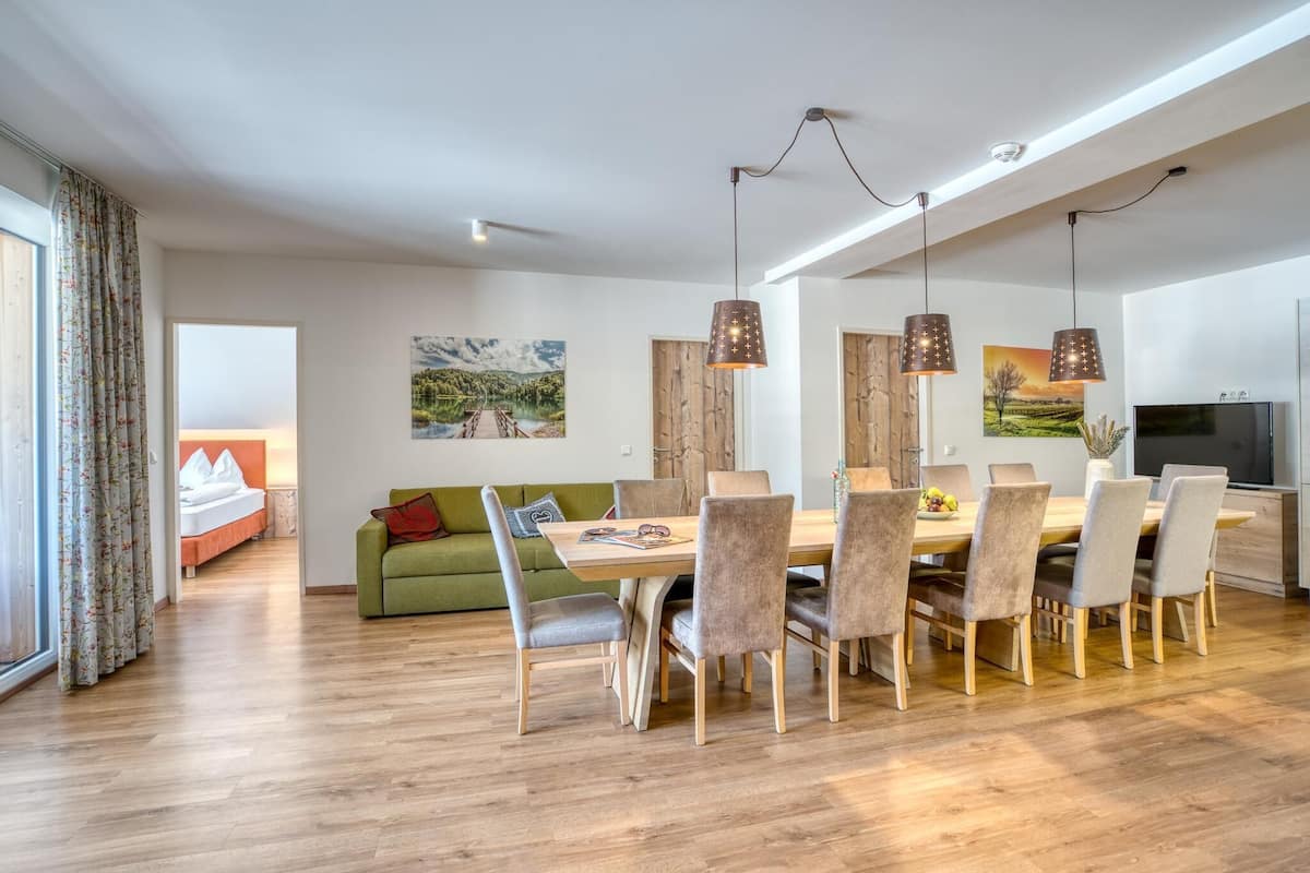 A modern living room with a dining area, wooden flooring, and a large window with curtains.