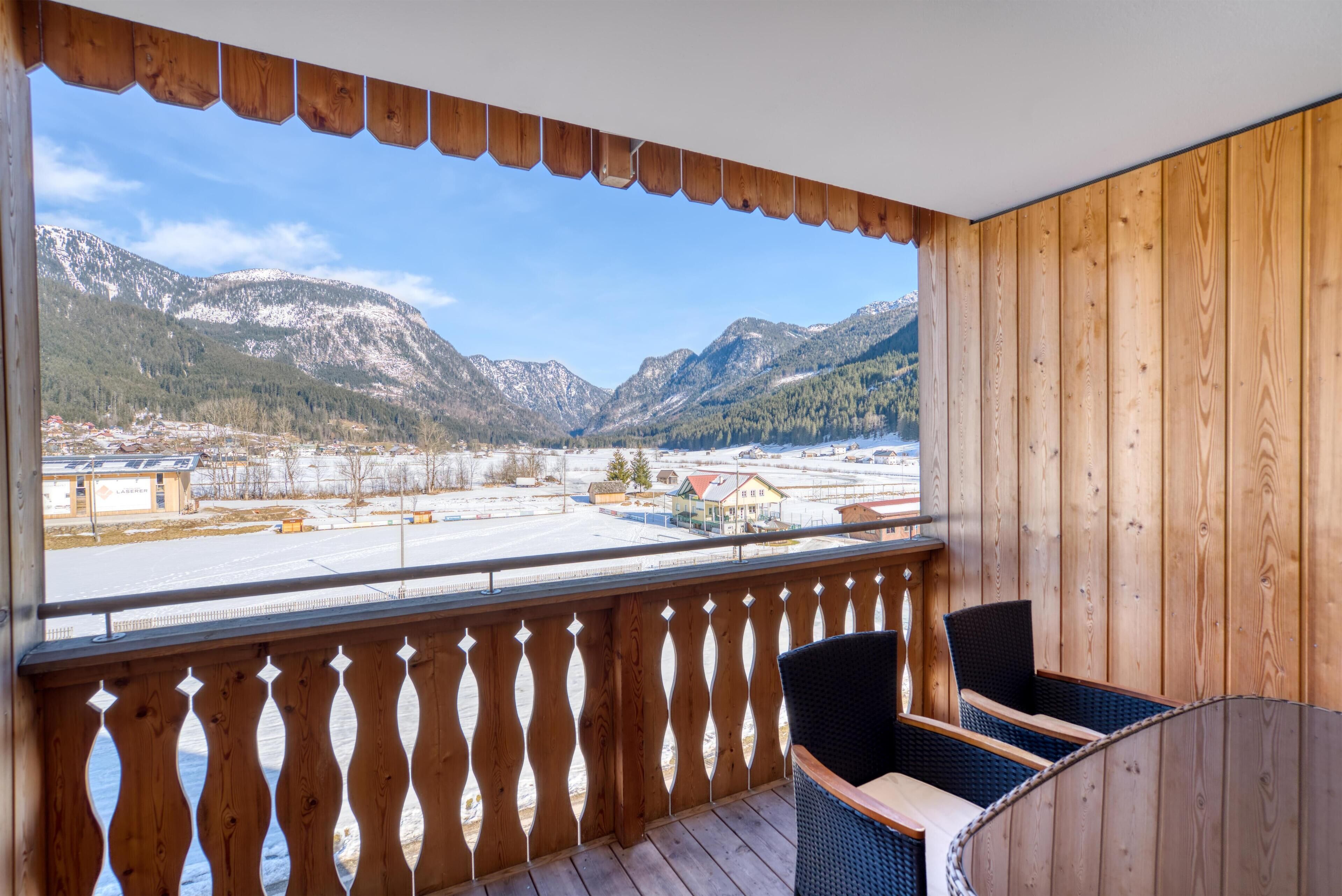Un balcón de madera con vista a montañas nevadas y un pueblo abajo.