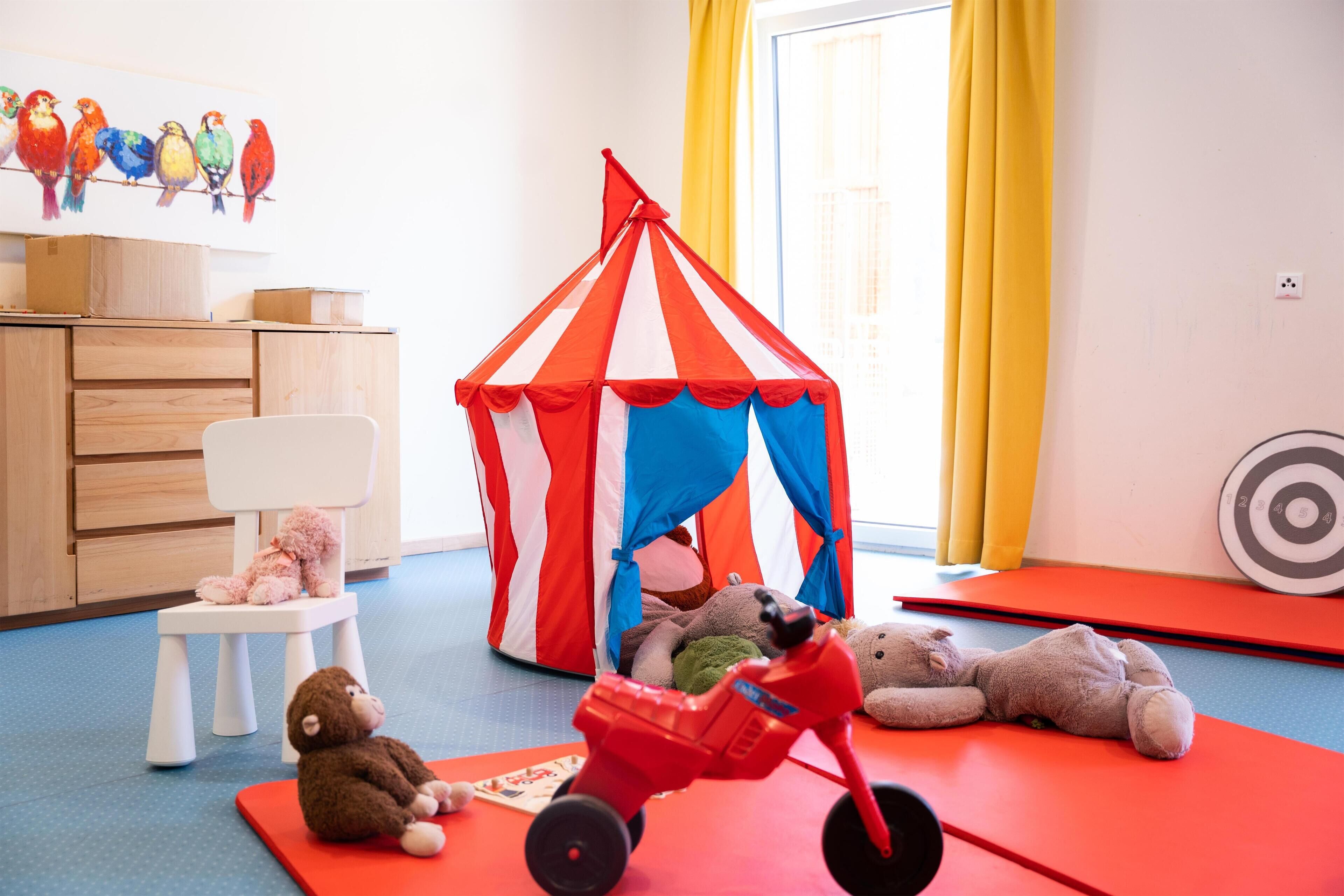 Ein Spielzimmer mit einem rot-weiß gestreiften Zelt, einem kleinen weißen Stuhl und einem roten Spielzeugauto.