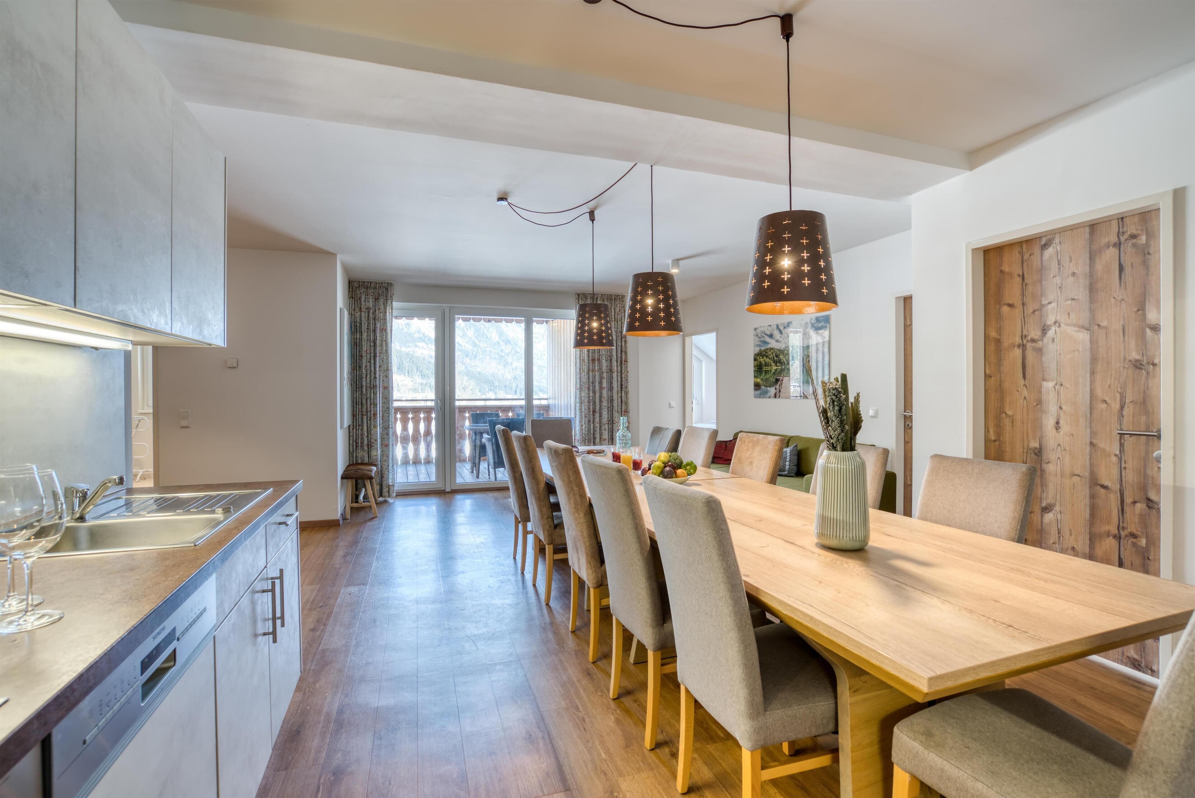 Een moderne keuken met een houten eettafel, grijze stoelen en hanglampen.