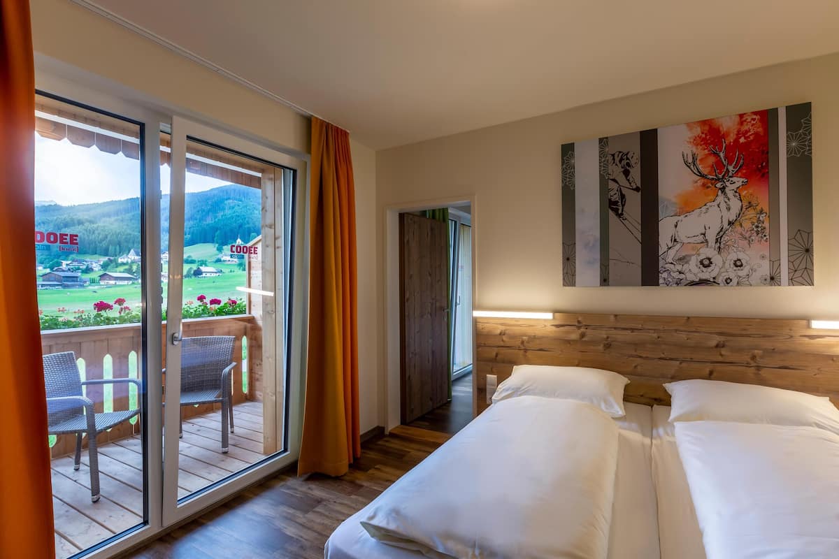 A hotel room with a bed, a balcony with chairs, and a painting on the wall.