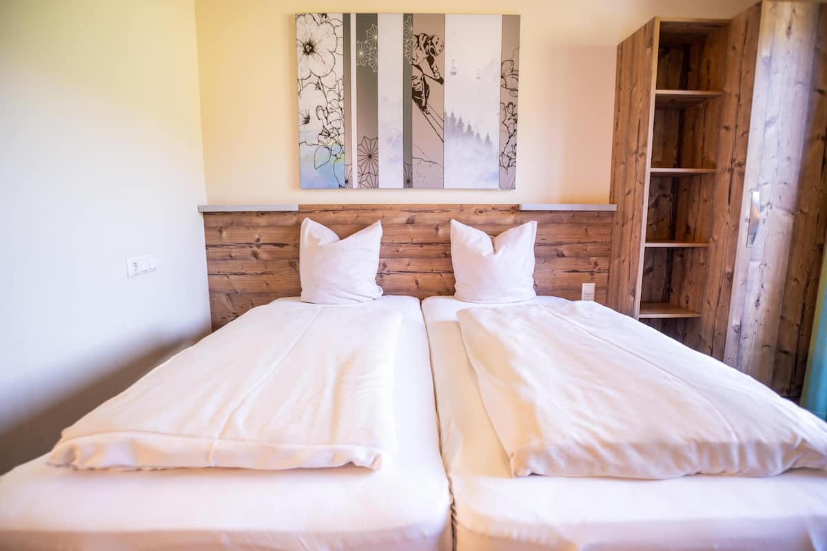 A room with two single beds, a wooden headboard, a wall-mounted artwork, and a wooden wardrobe.