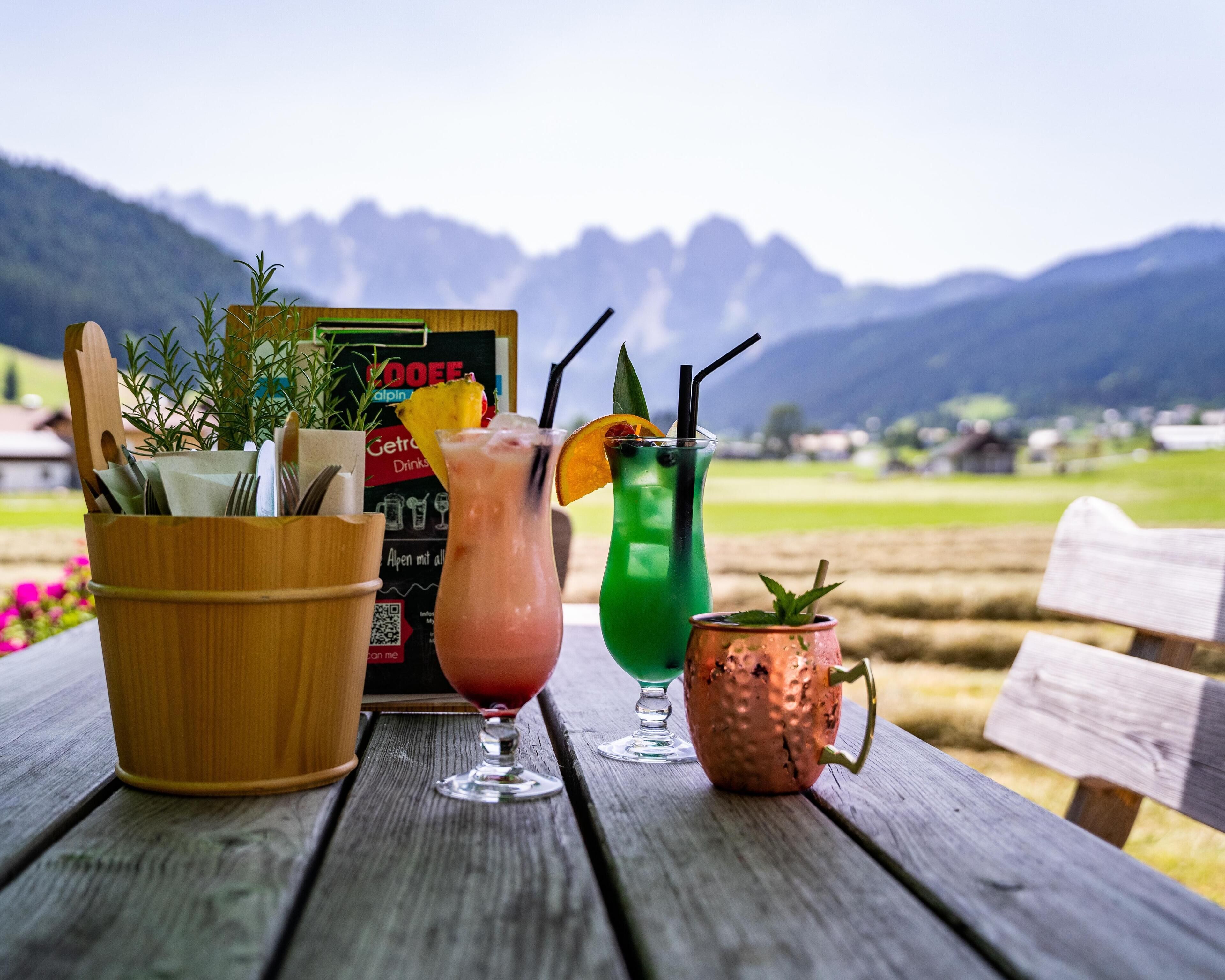 Een houten tafel met drie drankjes, een menukaart en een houten emmer met bestek.