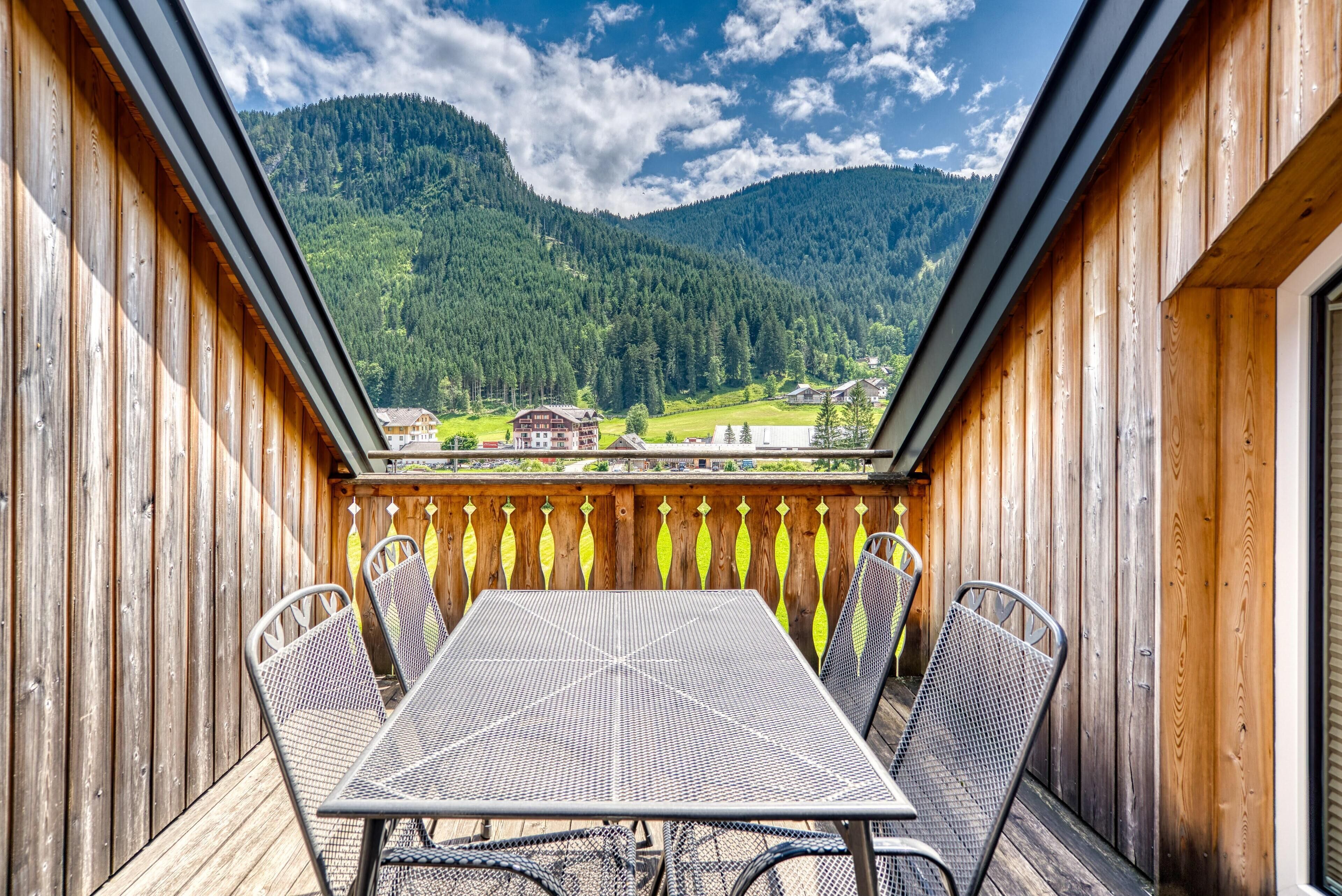 A wooden deck with a metal table and chairs, overlooking a mountainous landscape.