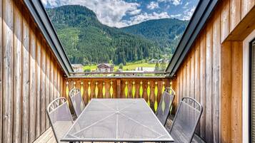 A wooden deck with a metal table and chairs, overlooking a mountainous landscape.