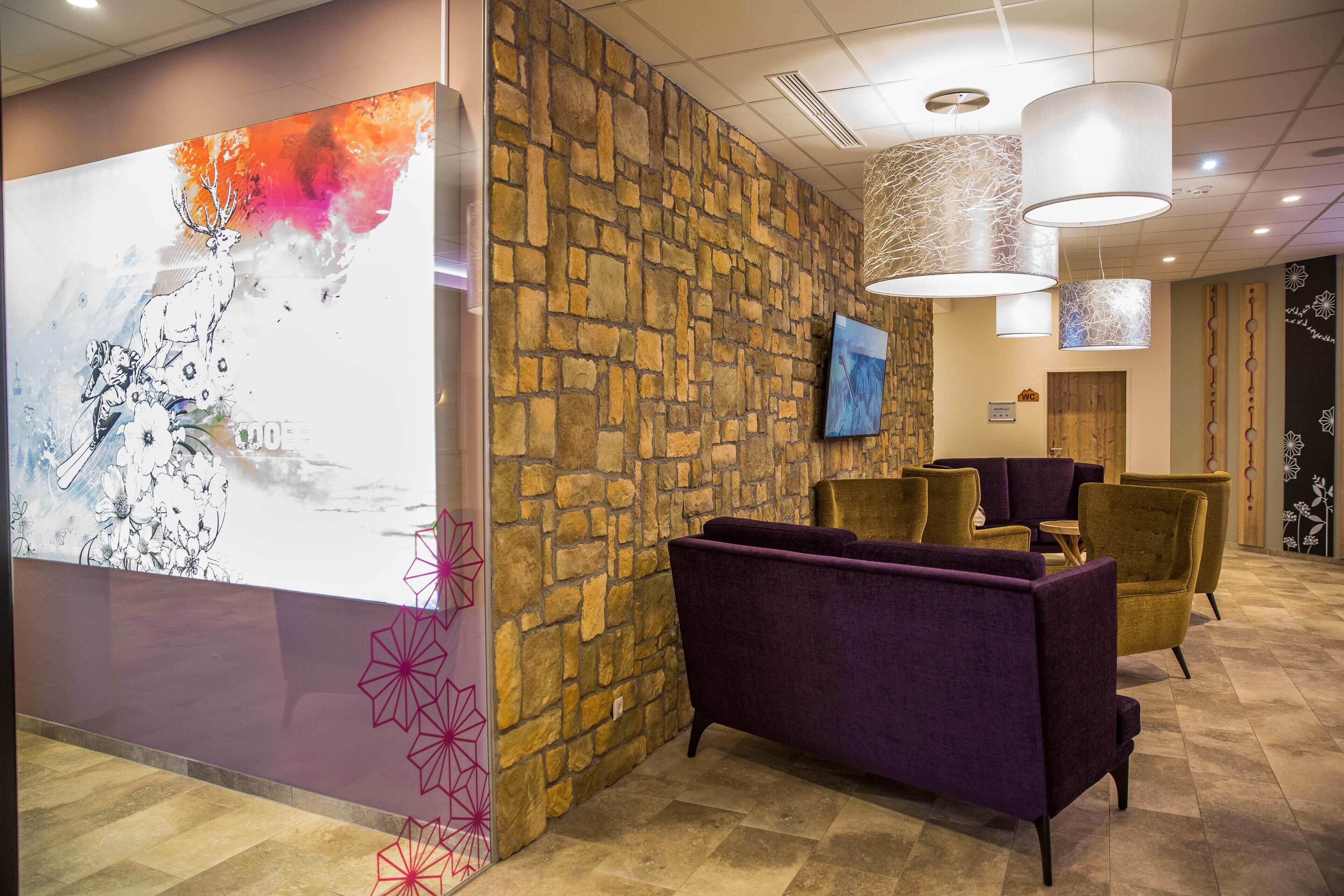 A lobby with a stone wall, purple and gold seating, and a large abstract painting.
