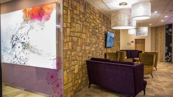 A lobby with a stone wall, purple and gold seating, and a large abstract painting.