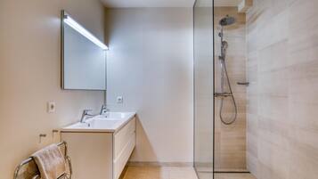 Un baño moderno con cabina de ducha de vidrio, un lavabo blanco y un espejo con iluminación integrada.