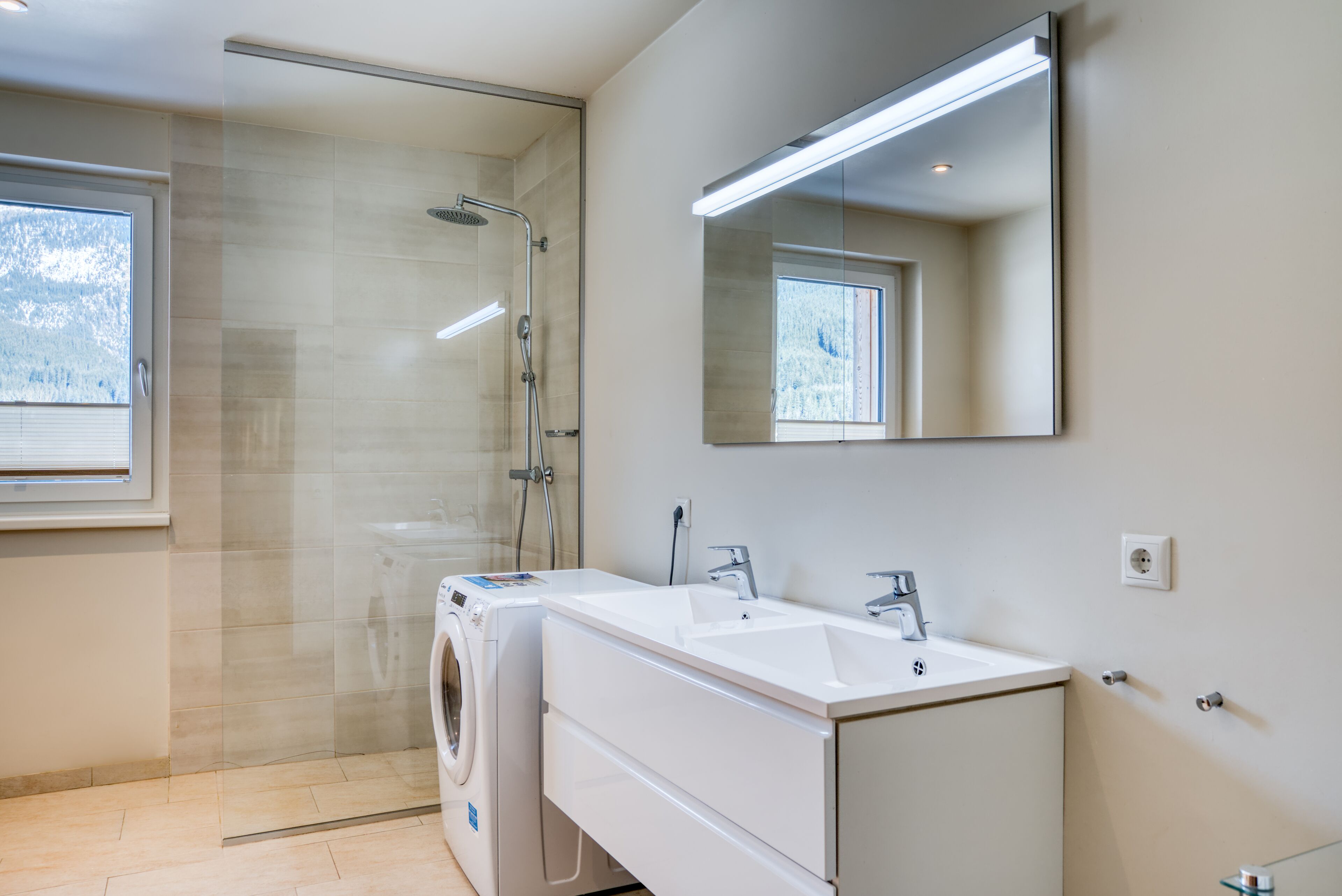 A modern bathroom with a glass shower enclosure, a built-in washing machine, and a large mirror above the sink.