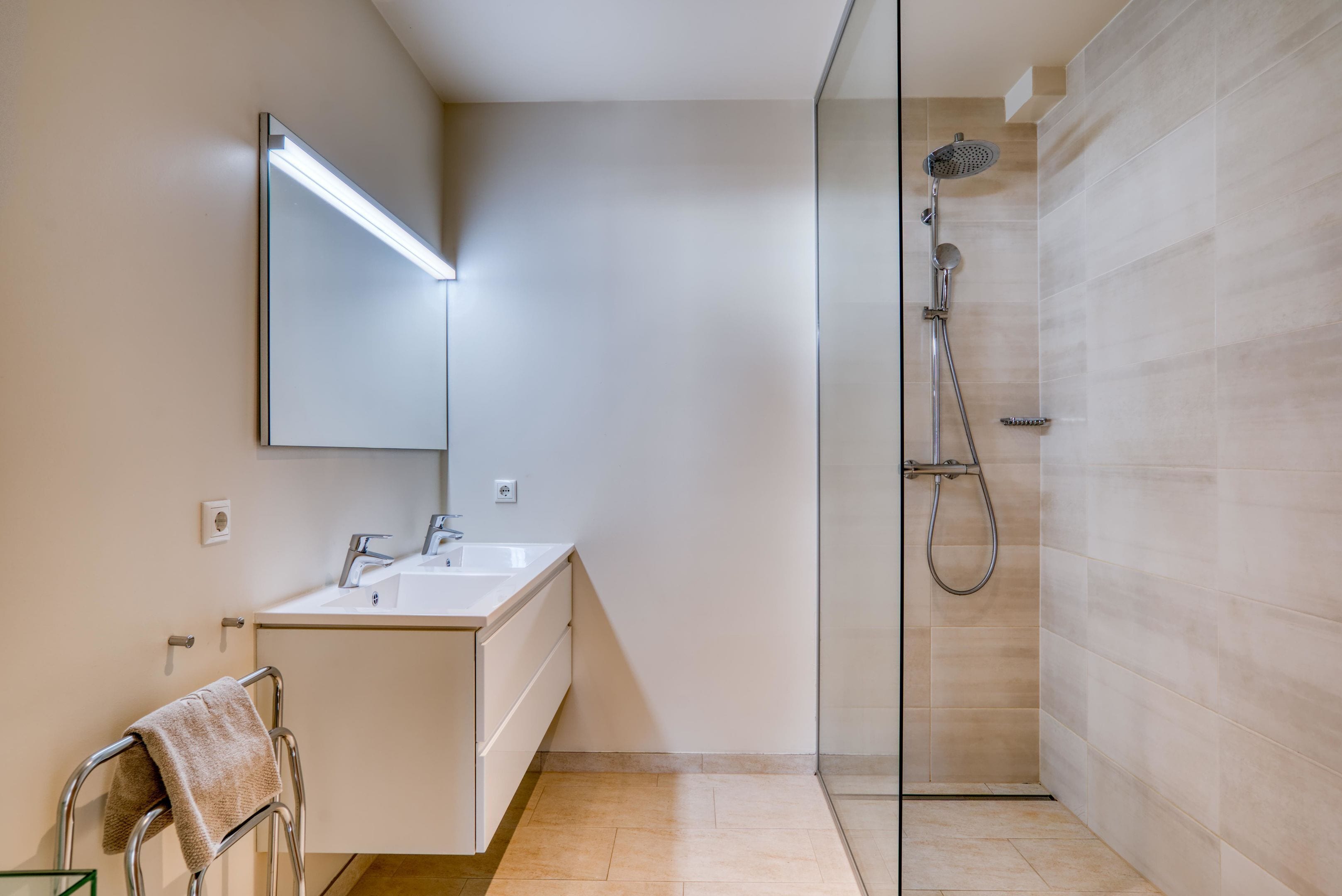 A modern bathroom with a glass shower enclosure, a white sink, and a mirror with integrated lighting.