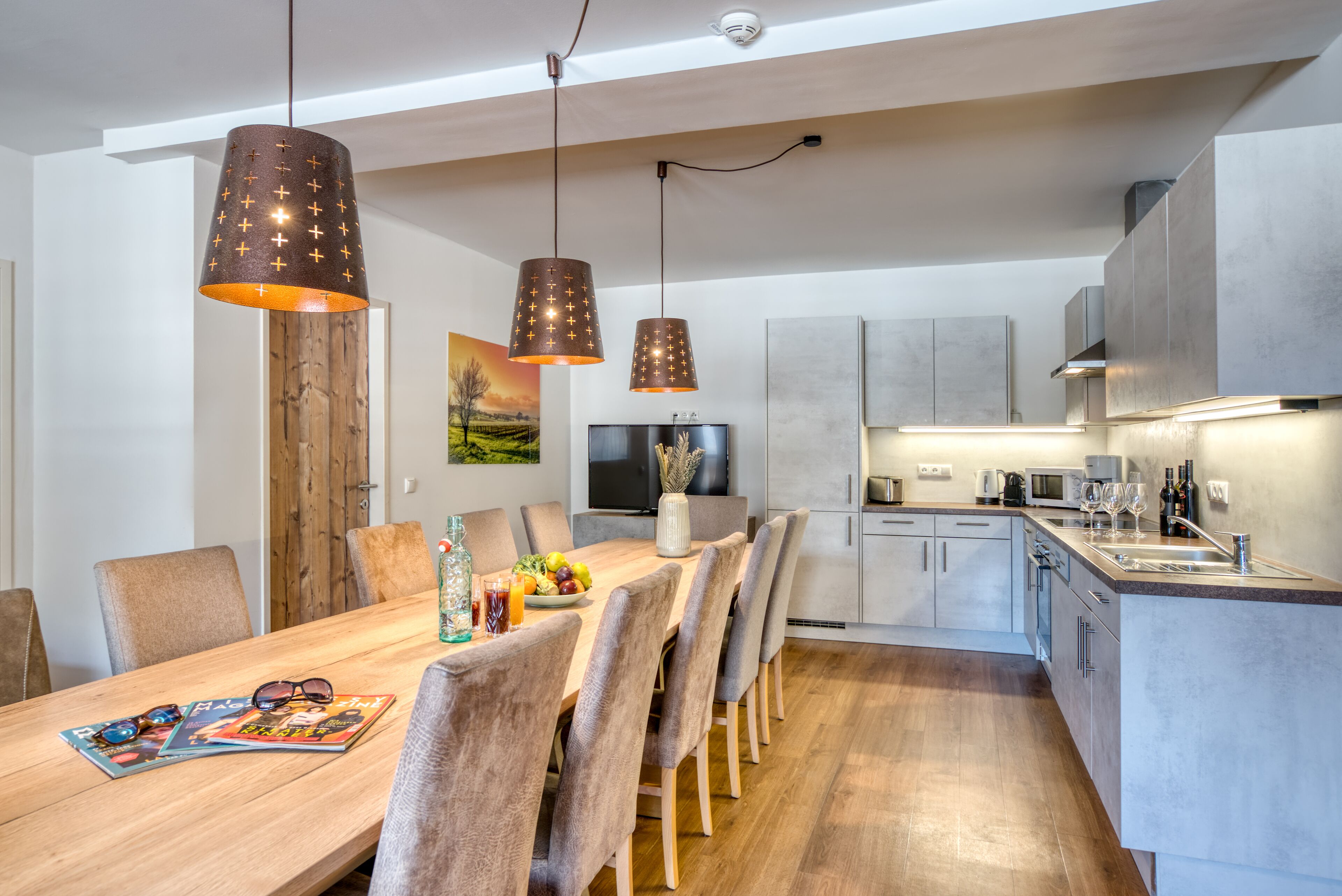 Una cocina moderna con una mesa de comedor de madera, sillas grises y luces colgantes.