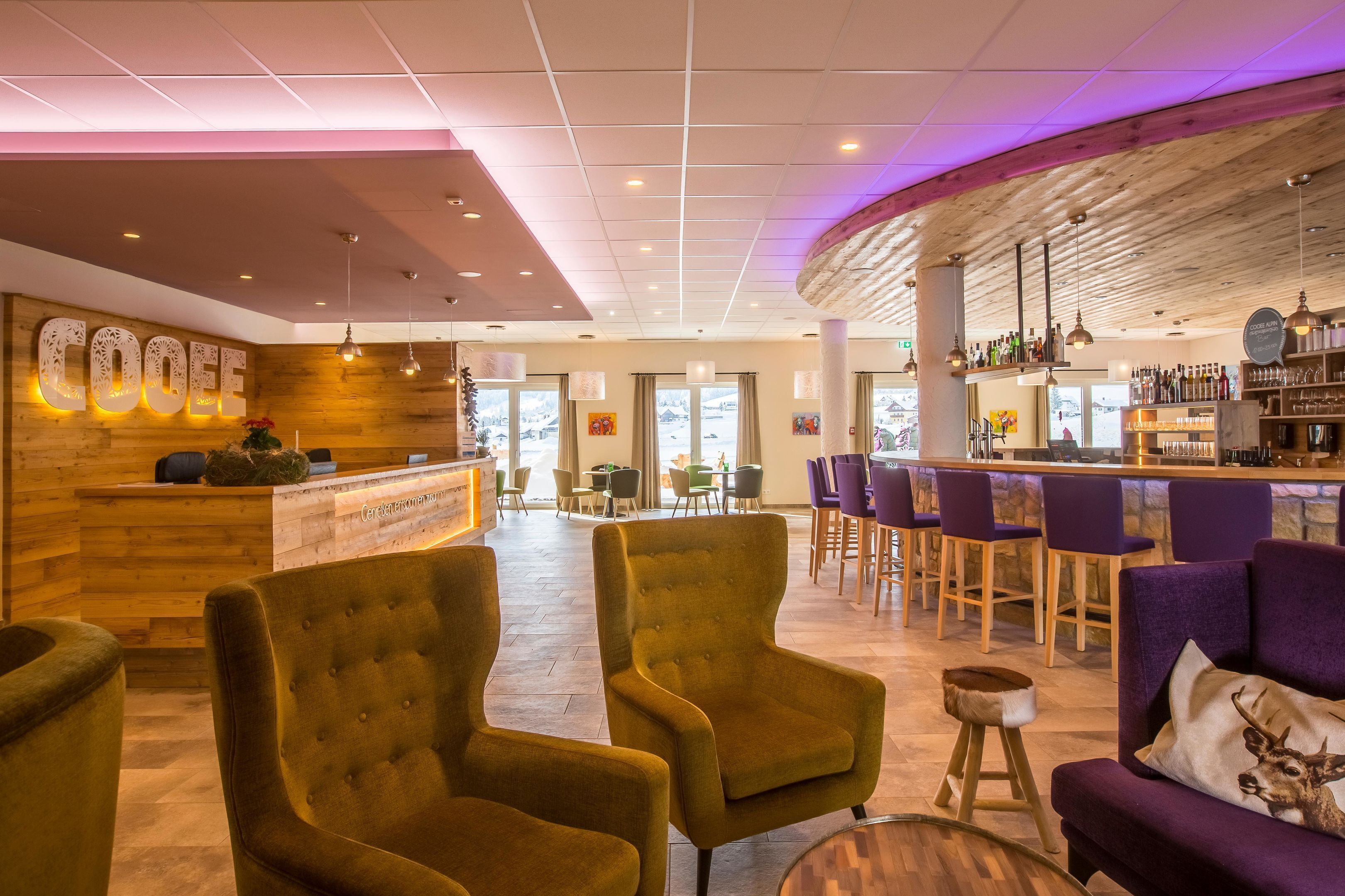 A bar area with a wooden reception desk, multiple seating options including bar stools and cushioned chairs, and a visible bar counter with bottles.