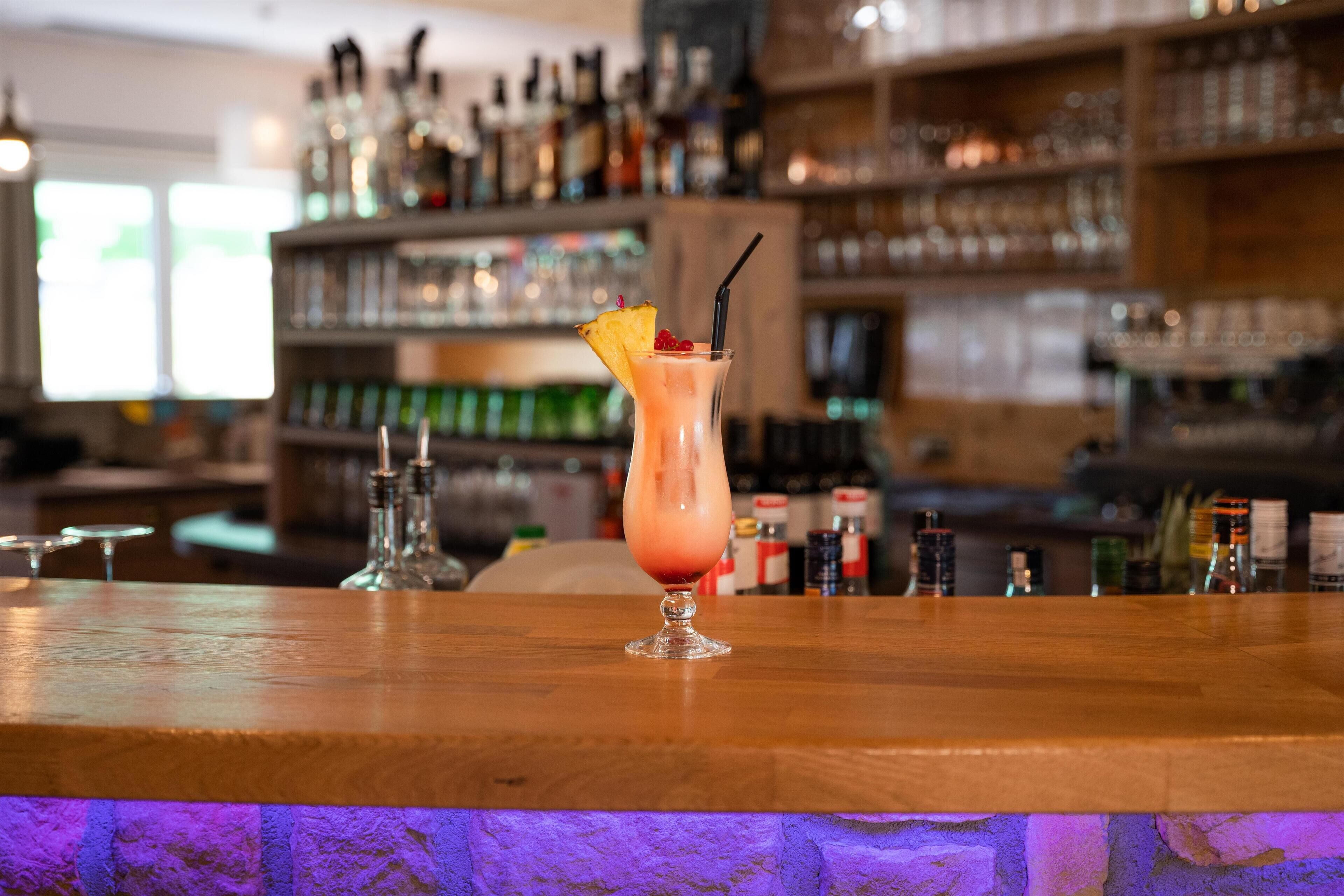 A bar area with a drink on the counter, shelves with bottles, and a bar counter.