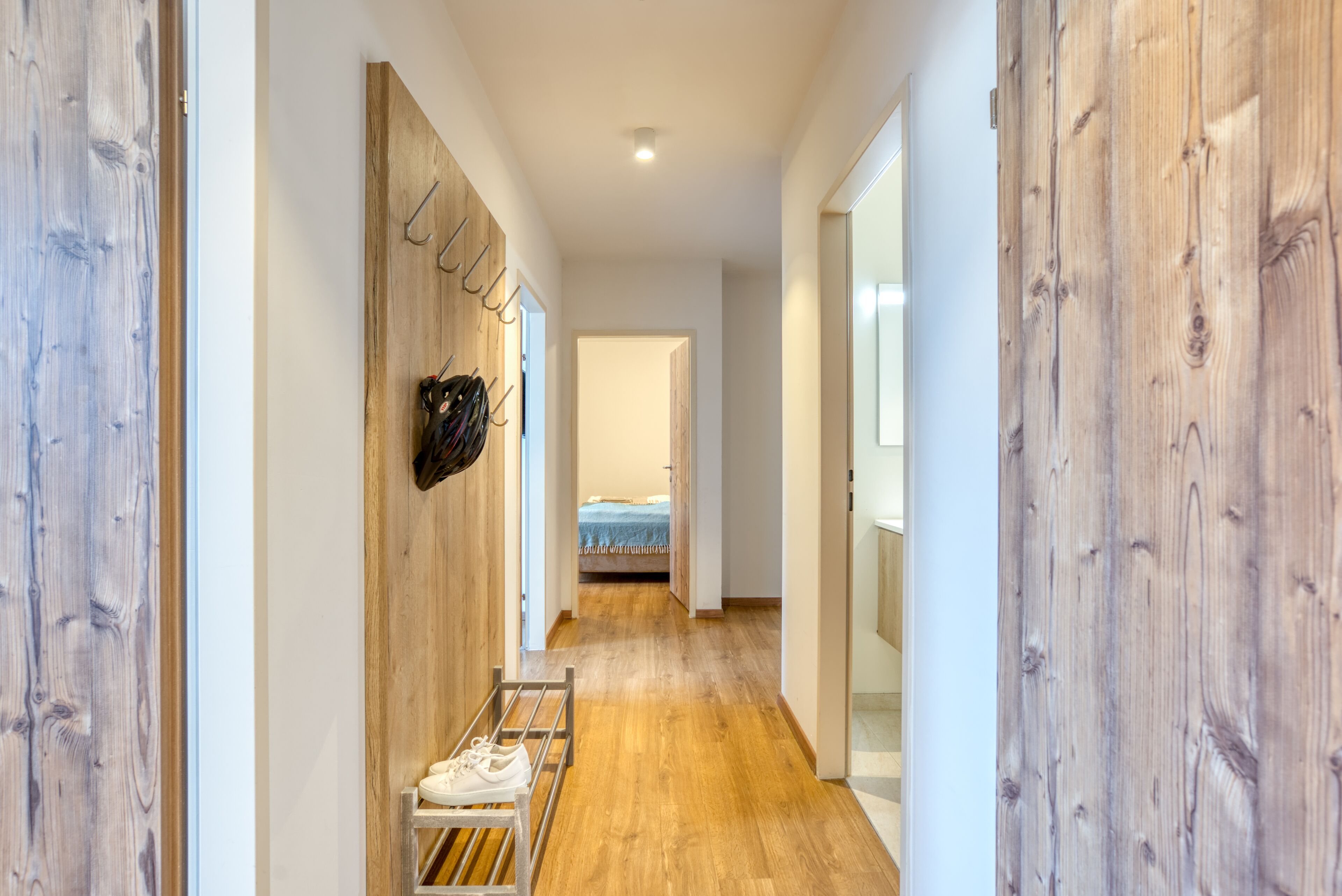 A hallway with wooden walls, a metal rack with shoes, and a bed in the distance.