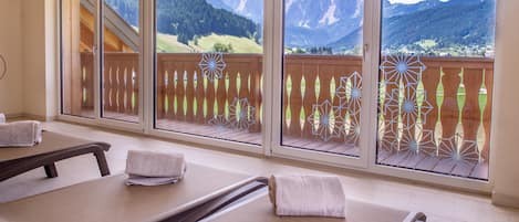 Una habitación con mesas de masaje, ventanas grandes con marcos de madera y vista a las montañas.