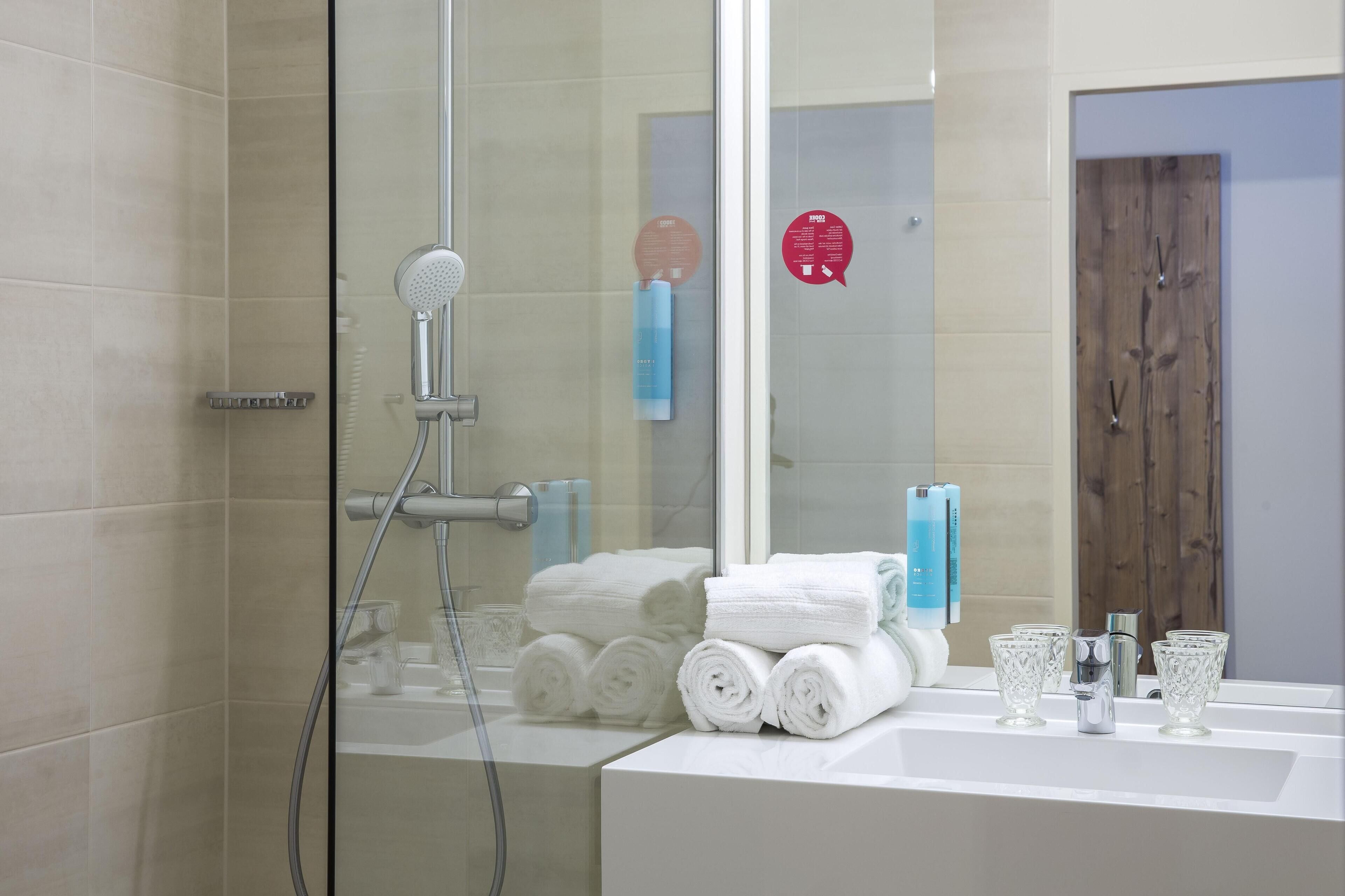 Un baño moderno con cabina de ducha de vidrio, toallas blancas y artículos de aseo en la encimera.