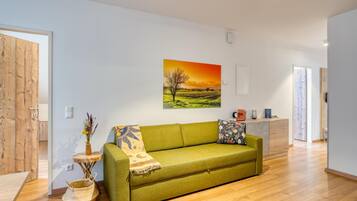 Ein modernes Wohnzimmer mit einem grünen Sofa, einem Sonnenuntergangsgemälde und einem Holzboden.