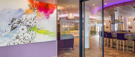 A modern interior with a large abstract painting, a bar area with purple chairs, and a visible sign for 'Cooler Lounge'.